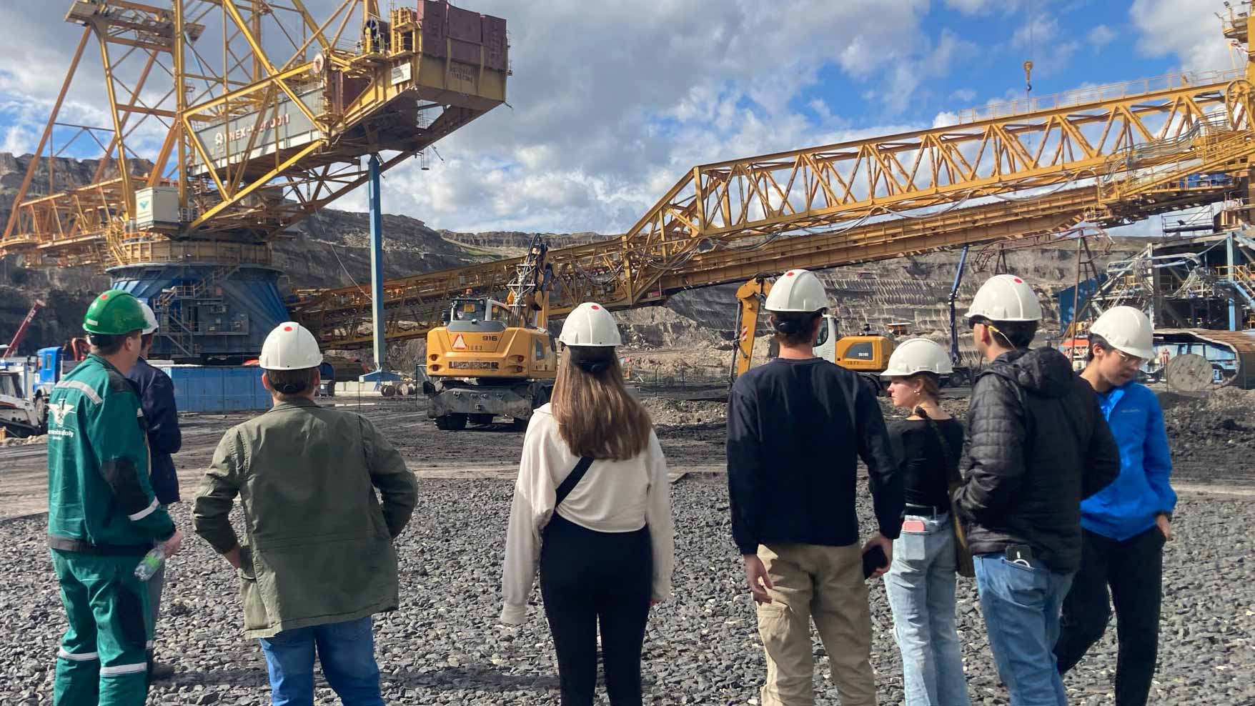 Students wearing helmets looking at gigantic crane in a coal mine