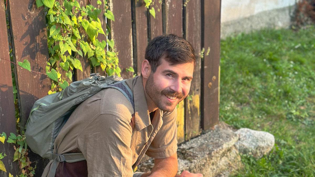 NC State Prague male student sitting and smiling at the camera with a garden in the background.