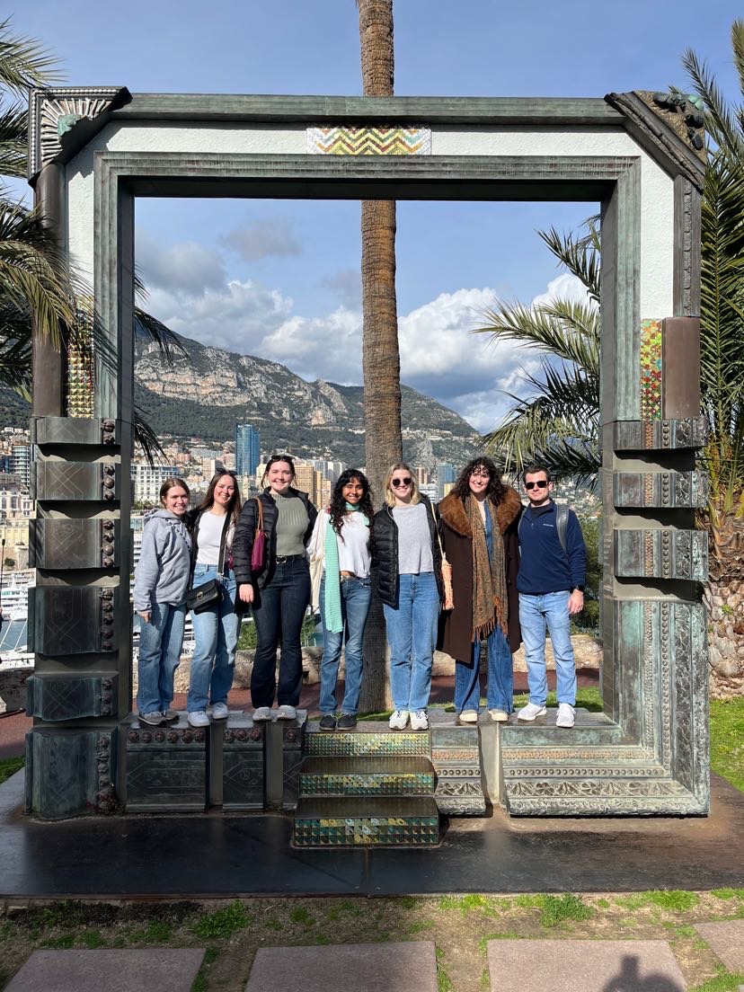 A group of eight students posing with Nice in the background.