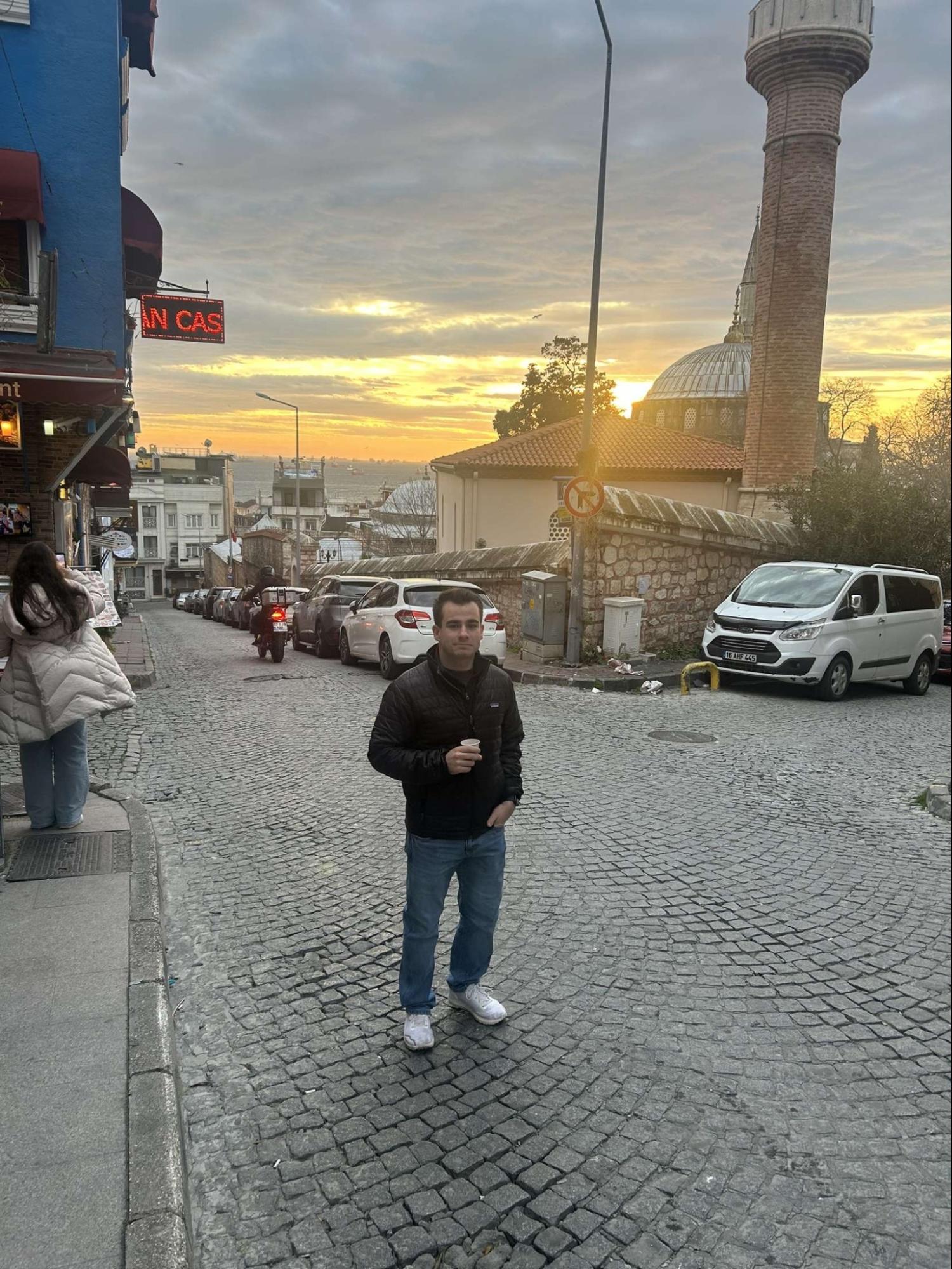 Eli stands on a cobblestone street in Prague during sunset.
