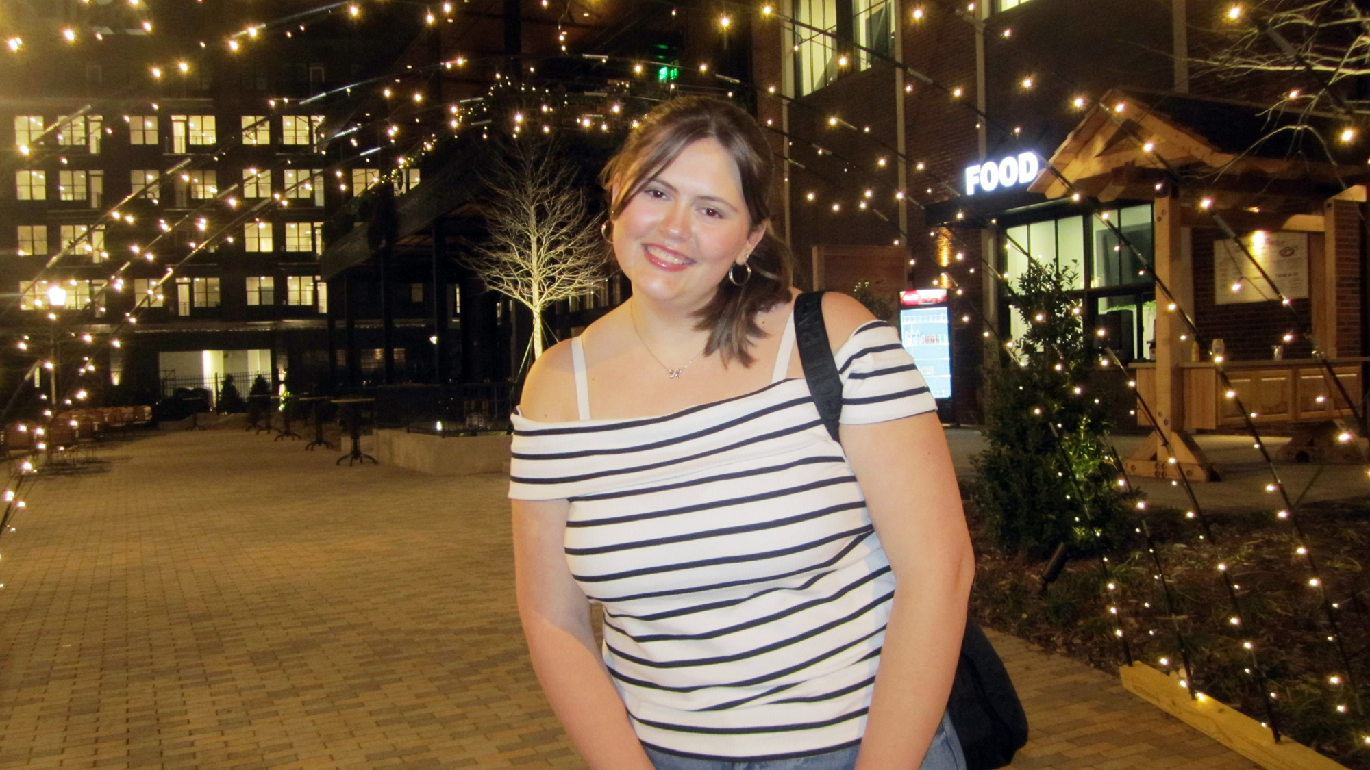 Isabel smiling at the camera at night with lights in the background.