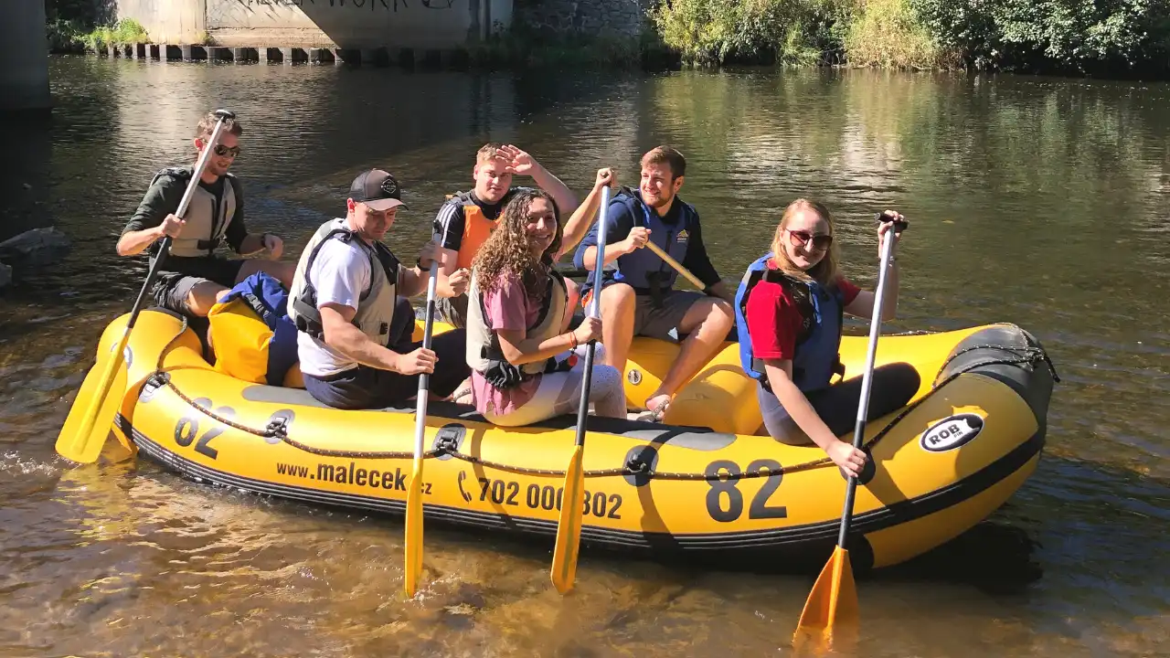 Bunch of smiling students on a yellow raft on the Vltava river.