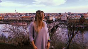 A student, Sydney, in a park at sunset with Prague's rooftops in the background