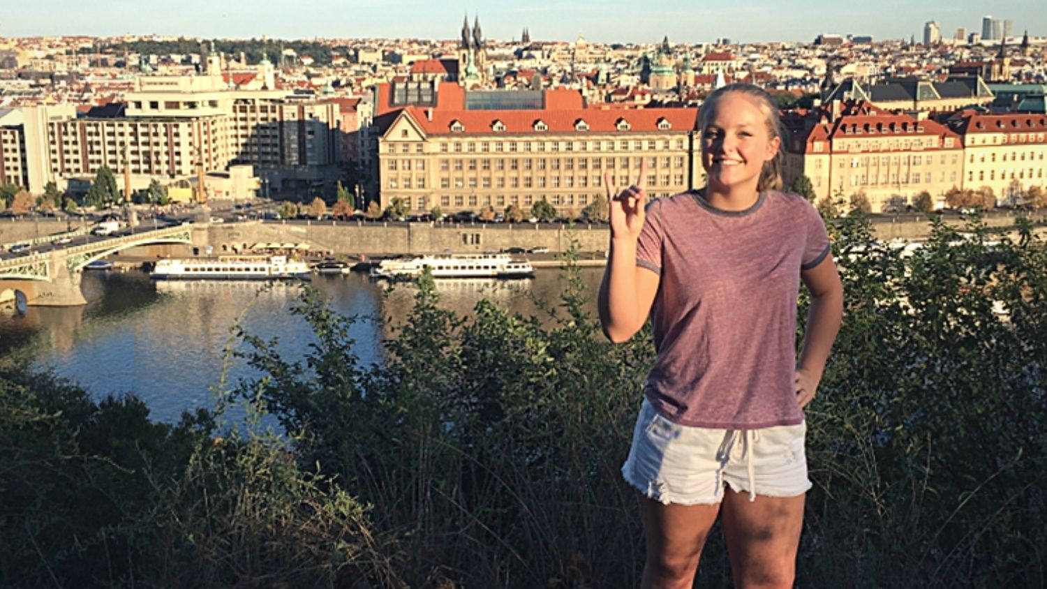 A student, Shea, making a wolfie with her hand with Prague's rooftops in the background.