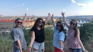 A student, Erica, wit three of her friends in a park with Prague's rooftops in the background