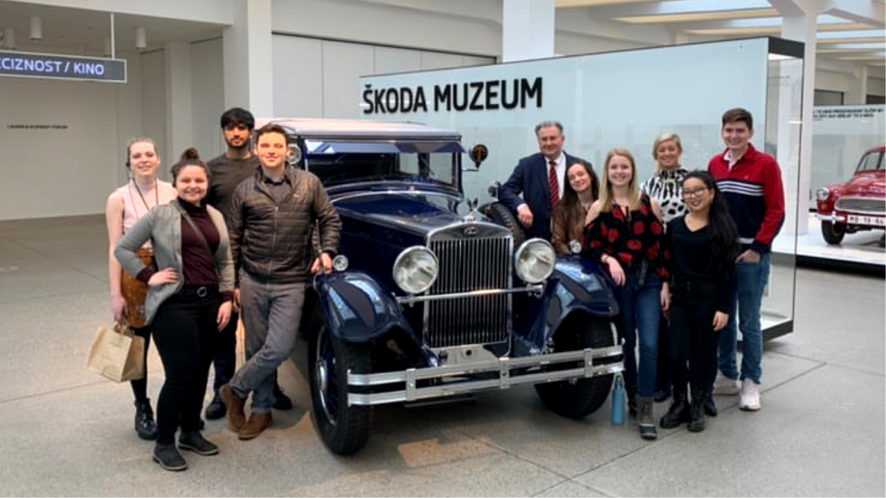 Group of American students smiling around an old Skoda car model at the Skoda car museum