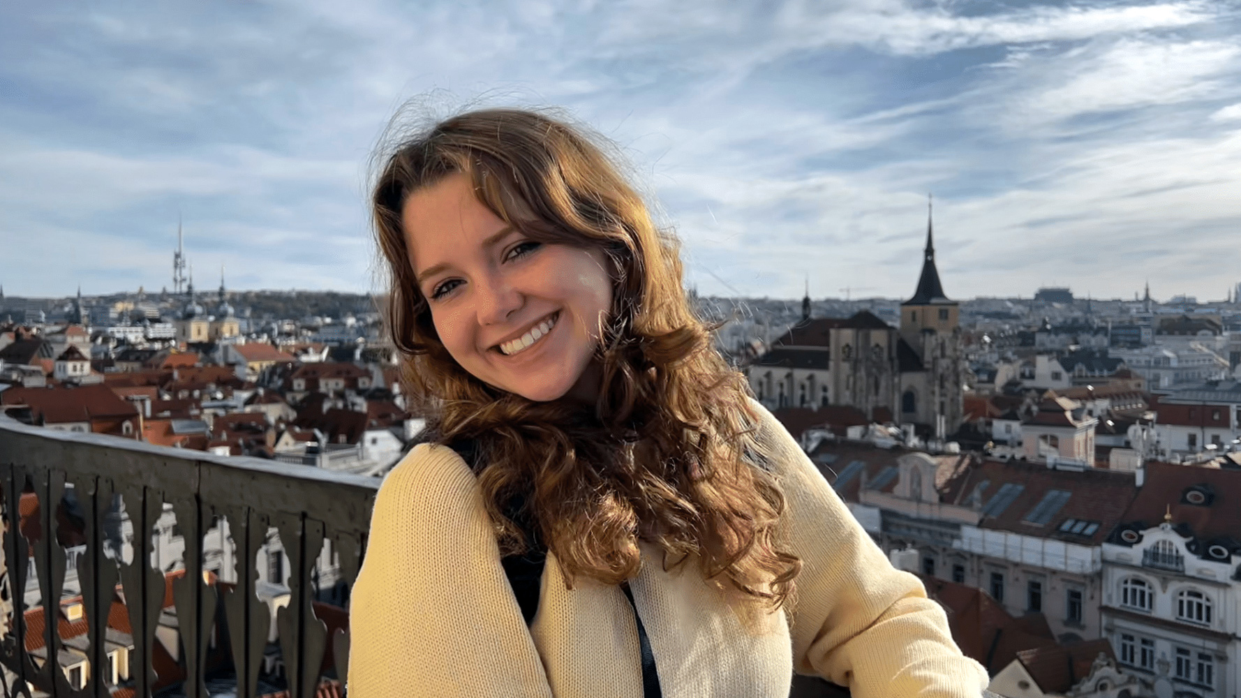 A student smiling posing with Prague cityscape in the background.