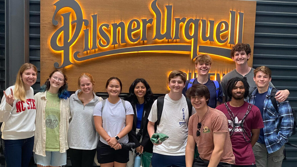 Group of students posing in front of Pilsner Urquell the sign