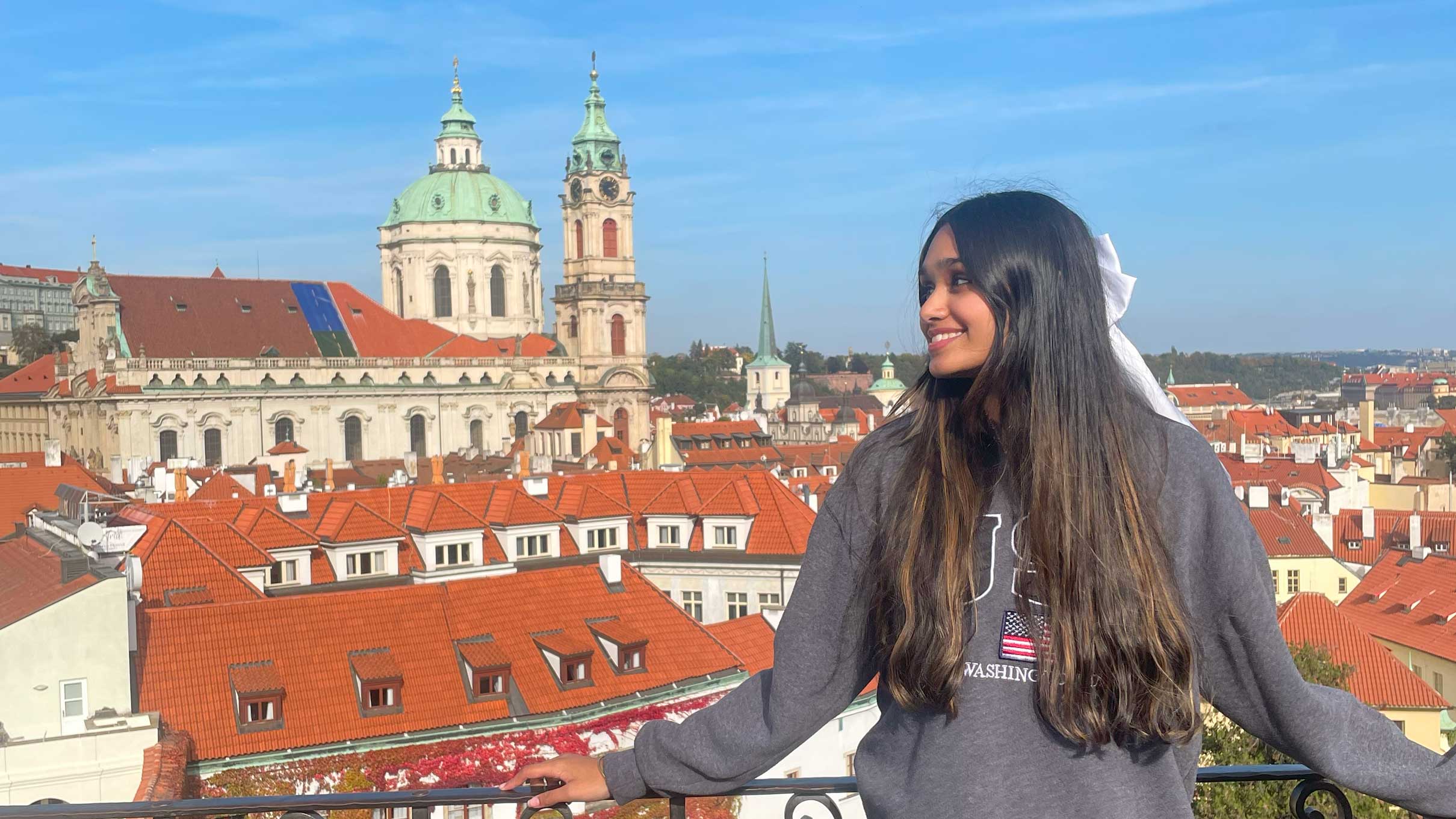 Aditi, a student on the Prague Connect program, looking on the side with Prague cityscpae in the background