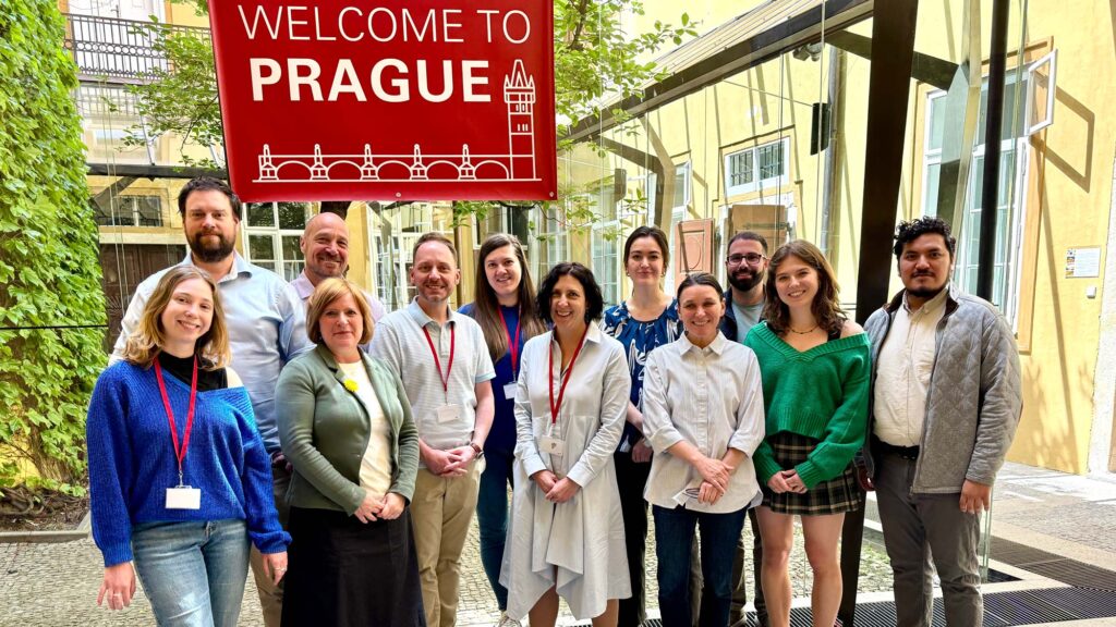 NC State Prague staff and guest in the courtyard of the Center under the red "Welcome to Prague" sign.